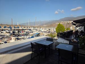Tables on a terrace above Radazul marina with mountains on the horizon.